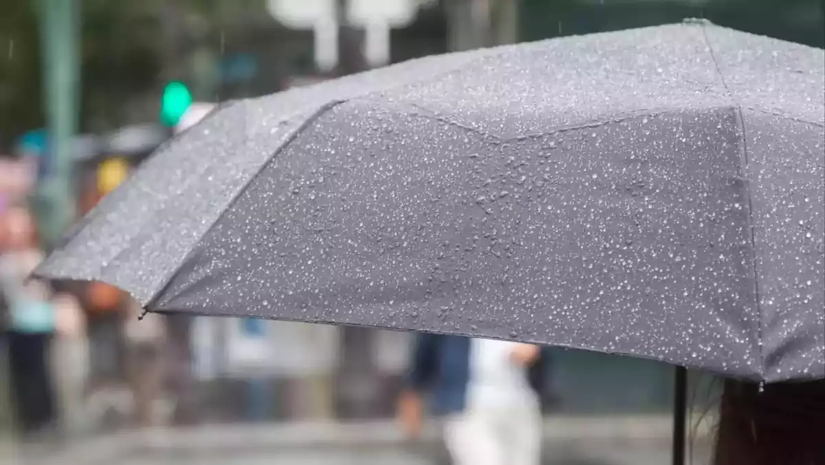 Una persona en primer plano bajo un paraguas con lluvia cayendo.